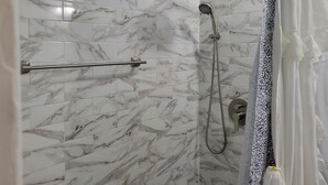 Een douche met een handdouche en een slangdouche, een handdoekhouder en een douchegordijn met een patroon.