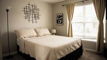 A bedroom with a large bed, a floor lamp, a wall art piece, and a window with curtains.