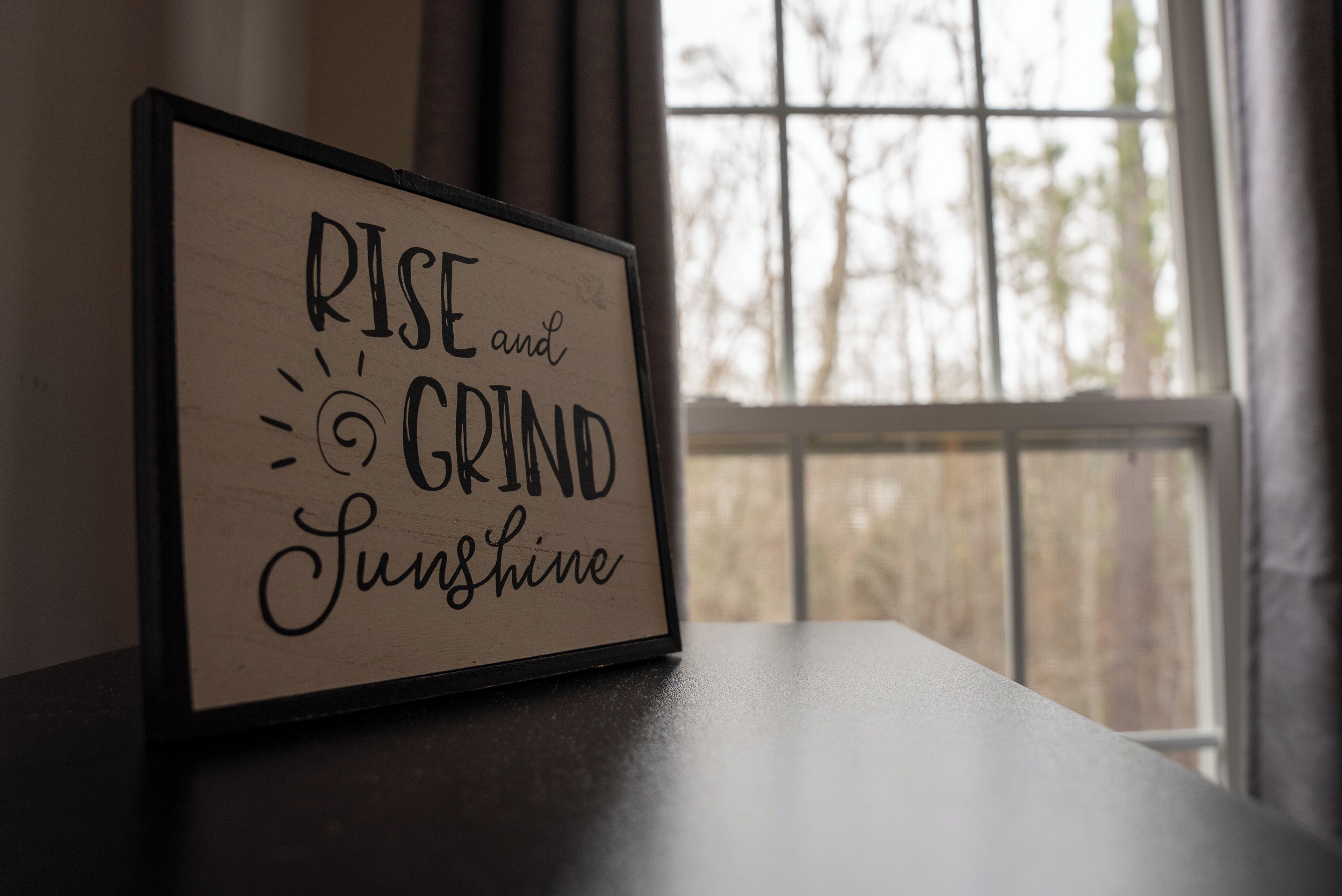 A framed inspirational quote on a table near a window.