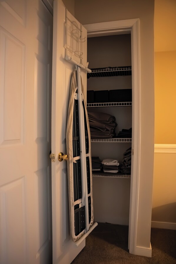 Un placard avec des étagères et une tringle pour suspendre les vêtements, une porte dotée d’une poignée de porte en laiton et un sol recouvert d’une moquette.