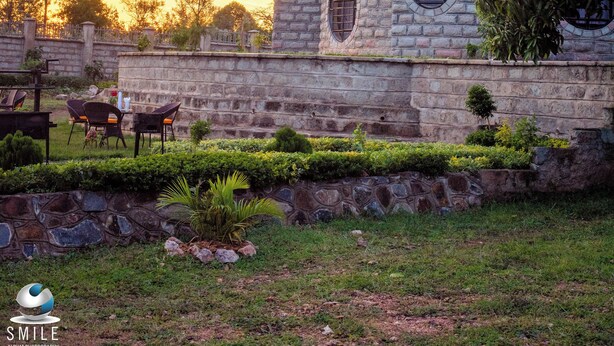 A building with a stone facade, a tiled roof, and a small garden area with chairs and tables. - Turaco Intercounty Resort Limited  (Kisumu)