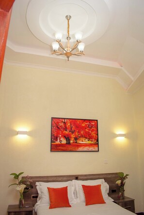 A hotel room with a bed, a painting of autumn trees, and a chandelier. - Turaco Intercounty Resort Limited  (Kisumu)