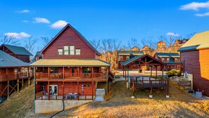 Un bâtiment de style chalet en bois, doté d’un balcon, d’une terrasse couverte et d’un petit espace extérieur aménagé pour s’asseoir.