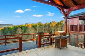 Eine Terrasse mit Grill und Stühlen mit Blick auf eine bewaldete Gegend.