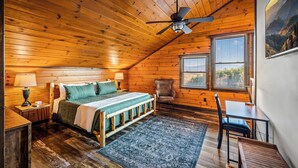 Une chambre confortable, aménagée dans un chalet en bois, avec un lit, une chaise, un bureau et un ventilateur de plafond.