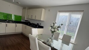 Una cocina moderna con armarios blancos, encimera negra y mesa de comedor de vidrio con sillas blancas.