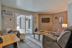 Un salon comprenant un canapé, une table basse et un téléviseur fixé au mur. Une porte-fenêtre coulissante donne accès à un balcon.