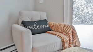 A light-colored sofa with a dark gray pillow that reads "welcome" and an orange patterned throw blanket. - Jelinek Hideaway Unit 5 - Modern 2BR Apartment (Schofield)