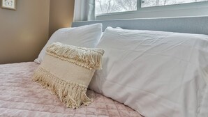 A bed with a pink quilted bedspread, a white pillow, and a beige macramé throw. - Jelinek Hideaway Unit 5 - Modern 2BR Apartment (Schofield)