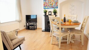 A cozy living room with a sofa, a TV, a fireplace, and a dining area with a table and chairs. - 3 Merlin Gardens Modern 2 Bed Bromley House (Bromley)