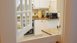 A kitchen with white cabinets, a microwave, and a window. - 3 Merlin Gardens Modern 2 Bed Bromley House (Bromley)