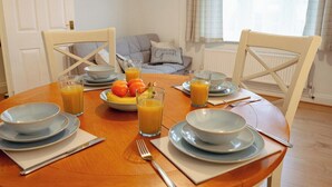 A dining table set with plates, bowls, and glasses of orange juice, with a bowl of fruit on the table. - 3 Merlin Gardens Modern 2 Bed Bromley House (Bromley)