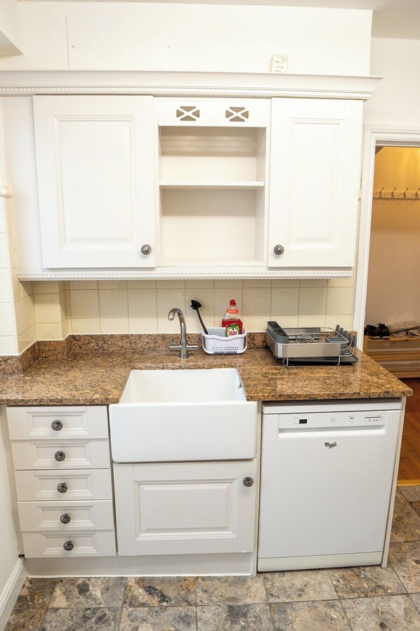 A compact kitchen with white cabinetry, a granite countertop, a sink, and a dishwasher.