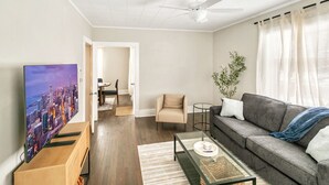 A modern living room with a flat-screen TV, a grey sofa, a glass coffee table, and a ceiling fan. - New updated home w/ porch and Fenced yard in DT Libertyville Near Naval Base (Libertyville)