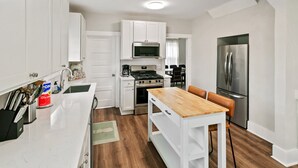 A modern kitchen with white cabinetry, a wooden dining table, and a stainless steel refrigerator. - New updated home w/ porch and Fenced yard in DT Libertyville Near Naval Base (Libertyville)