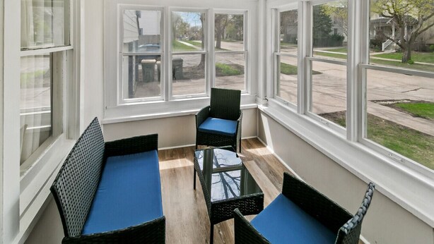 A sunroom with a view of a residential street, featuring wicker furniture and a glass table. - New updated home w/ porch and Fenced yard in DT Libertyville Near Naval Base (Libertyville)