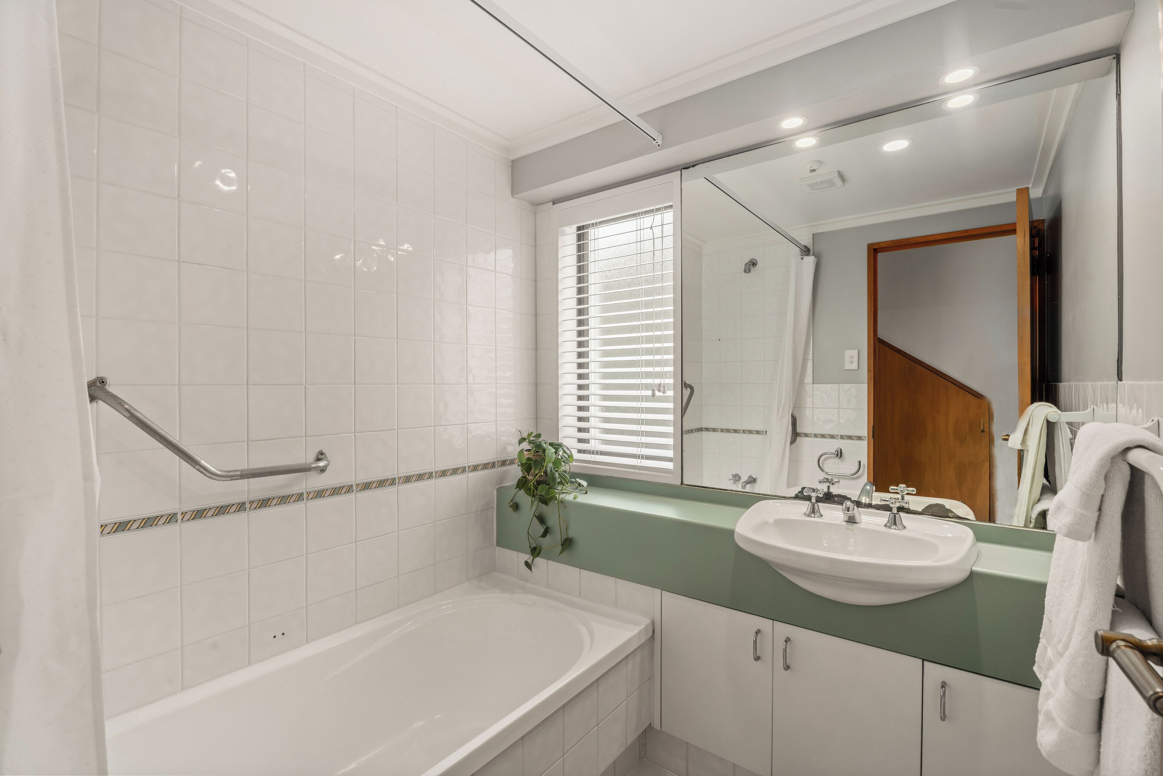 A modern bathroom with a white bathtub, a green vanity with a sink, and a large mirror.