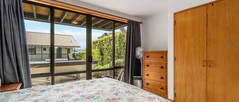 A bedroom with a large bed, wooden wardrobe, and a view through a sliding door to the outside.