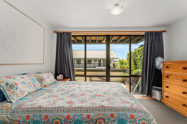 A bedroom with a large bed, a wooden dresser, and a sliding glass door leading to an outdoor area.
