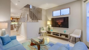 Una sala de estar moderna con una escalera, un televisor de pantalla plana y un comedor al fondo.