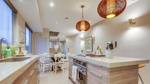 Una cocina moderna con una isla central, electrodomésticos de acero inoxidable y un comedor con sillas blancas.