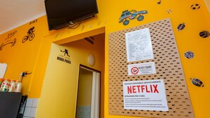 A room with a yellow wall, a mounted television, and a bulletin board with a Netflix sign. - Sports Cave (Torino)