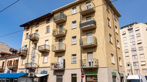 A multi-story building with balconies, a visible storefront, and a clear sky. - Sports Cave (Torino)