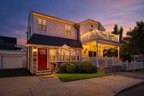 A two-story house with a red front door, a balcony, and a porch with string lights. - Ventnor Beach Gem: Central AC, Patio&Deck, Parking (Ventnor City)