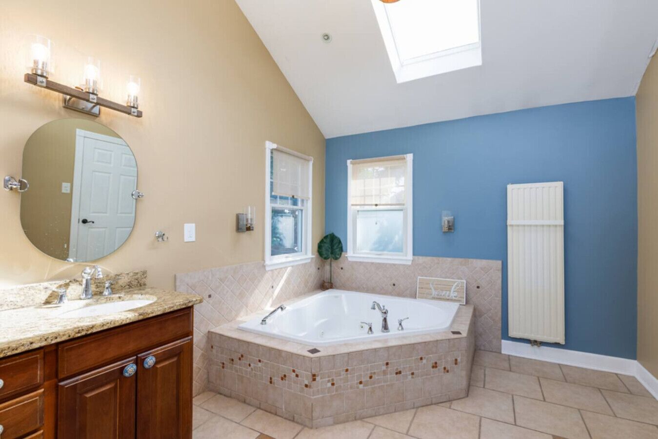 Un baño con una bañera grande, un espejo redondo, un tocador con lavabo y una ventana.