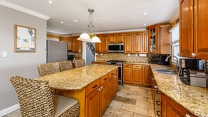 Una cocina con encimeras de granito, armarios de madera, una isla integrada y un comedor con sillas de mimbre.