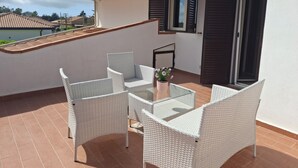 Un balcón con mobiliario de mimbre, una mesa de vidrio y una planta en maceta.