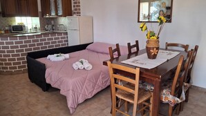 Una habitación acogedora con una cama, una mesa de comedor con sillas, una zona de cocina y un espejo en la pared.