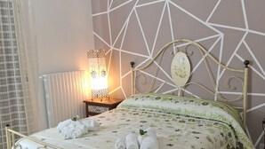 Una cama bien hecha con un edredón floral y toallas enrolladas, una pared con diseño geométrico y una mesita de noche con una lámpara.