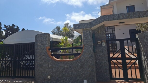 Una entrada cerrada con muro de piedra, portón metálico y un edificio con techo plano y un letrero con el número 28.