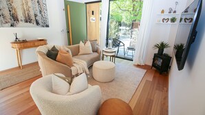 A cozy living room with a sofa set, a round ottoman, and a small side table. A wooden cabinet with a green panel and a sign that reads "Olive" is visible. - The Rocks - Olive Retreat (Bright)