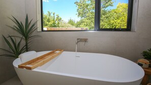 Une salle de bain moderne avec une baignoire sur pieds, un plateau en bois et une fenêtre donnant sur un paysage verdoyant.