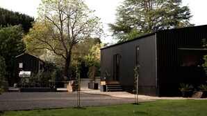 A modern building with a gravel driveway, surrounded by trees and a grassy area. - The Rocks - Olive Retreat (Bright)
