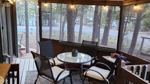 Un espacio al aire libre techado con una mesa redonda y sillas, un tapete estampado, y vistas a árboles y una carretera.