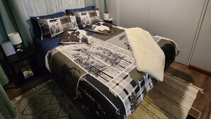 Un dormitorio con cama, ventilador de techo, mesita de noche, lámpara y un cuadro en la pared.
