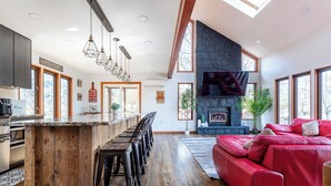 A spacious living area with a red sofa, a stone fireplace, and a large TV. - Rustic Ski Retreat! 2 min. walk to Ski Slopes, 6TVs, Linens, Wi-Fi, A/C, Firepit (bushkill)