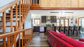 A spacious kitchen with wooden cabinets, a red sofa, and a staircase with wooden railings. - Rustic Ski Retreat! 2 min. walk to Ski Slopes, 6TVs, Linens, Wi-Fi, A/C, Firepit (bushkill)