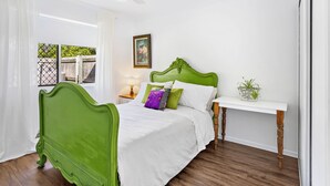 A bedroom with a green upholstered bed, white bedding, a bedside table with a lamp, and a small potted plant.
