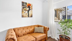 A brown leather sofa with a patterned pillow, a potted plant, and a painting on the wall.