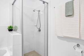 A modern bathroom with a glass shower enclosure, white tiles, a towel rack, and two potted plants.
