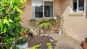 A brick house with a small garden area, including a metal table and chairs, and a window with a metal screen.