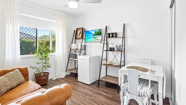 A compact living space with a sofa, a dining table, a small kitchen area, and a potted plant.