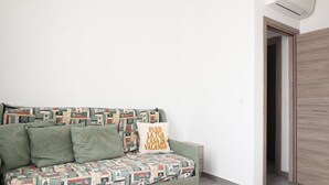 Quarto com sofá estampado, almofada com texto, porta de madeira e ar condicionado.