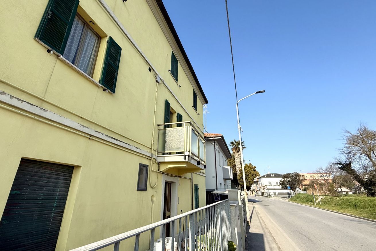 A yellow building with a balcony, a closed shutter, and a street in the background.