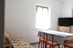 A room with a bed, a dining table with chairs, a television, and a window with curtains.
