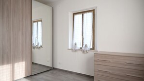 Quarto com um espelho grande, janela com cortinas, cômoda de madeira e piso ladrilhado.